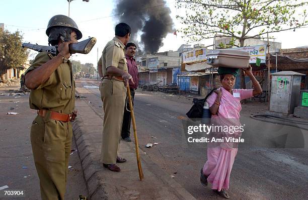 Indian police watch a Hindi woman carry her belongings on her head as she flees her home March 1, 2002 in Ahmadabad, India, two days after a Muslim...