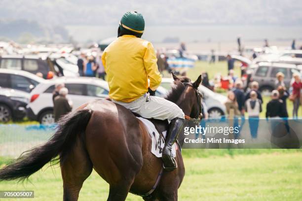 rear view of a jockey in a yellow vest riding a race horse. - purebred stock pictures, royalty-free photos & images