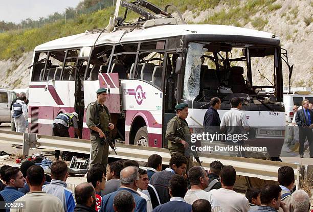 Israeli Arabs watch as police investigators inspect a passenger bus destroyed by a Palestinian suicide bomber March 20 who blew himself up on the bus...