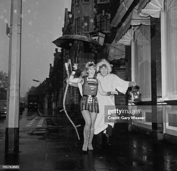 Actors Carol Dilworth and Christopher Timothy share an umbrella on a rainy New Year's Day in London, 1st January 1968. Timothy is dressed as Old...