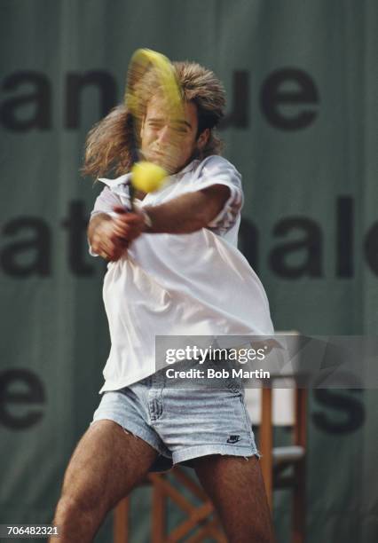 Andre Agassi of the United States wearing his jean style shorts makes a double hand return during a Men's Singles match during the French Open Tennis...