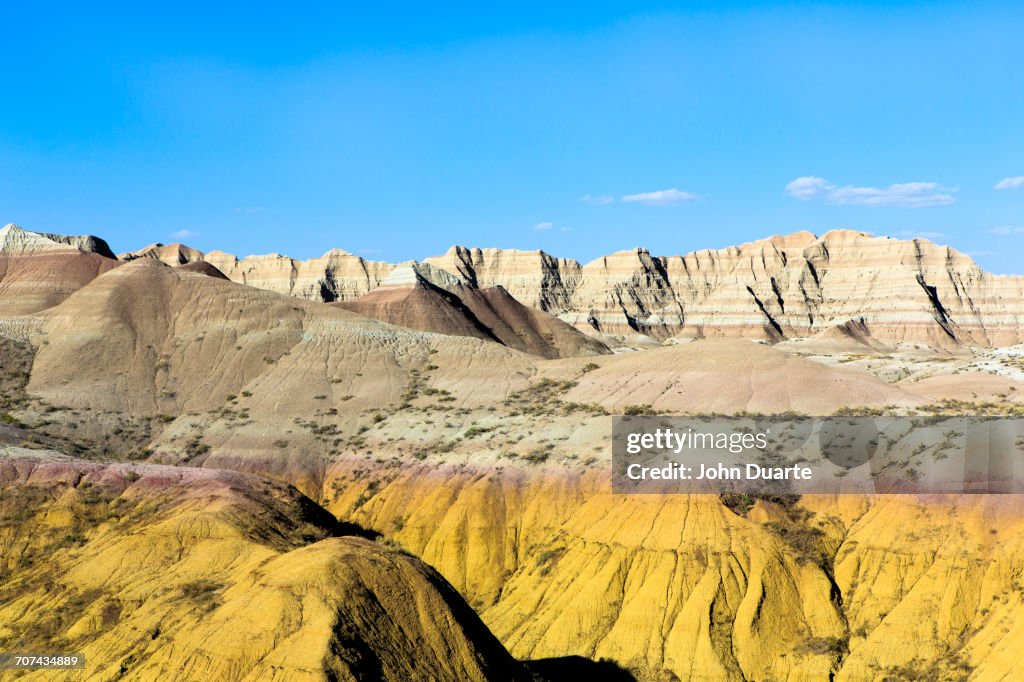 Layered rock formations under blue sky, Badlands National Park, South Dakota, United States