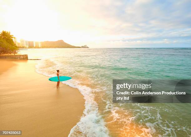 pacific islander woman holding surfboard on beach - oahu stockfoto's en -beelden