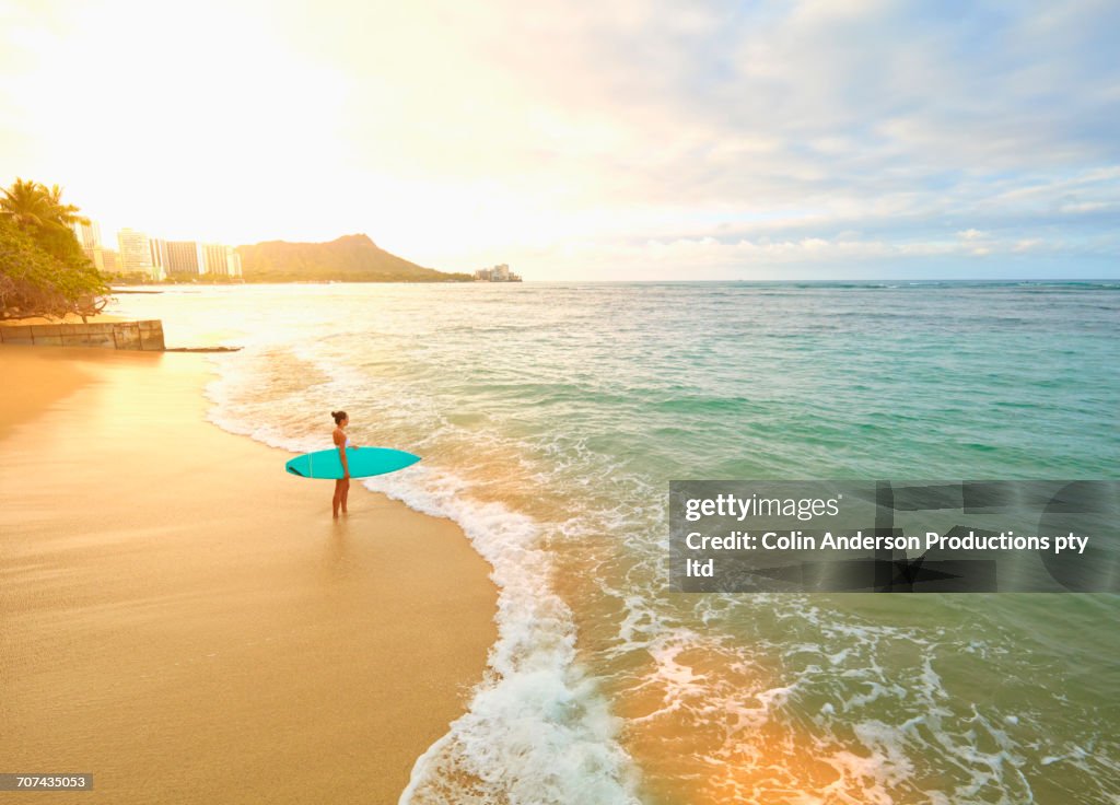 Pacific Islander woman holding surfboard on beach