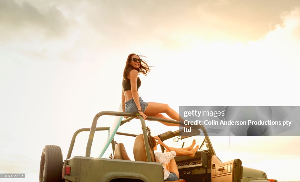 Women relaxing in off-road vehicle with surfboard