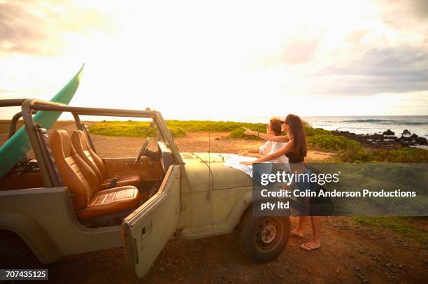 women leaning on off-road vehicle with surfboard reading map - innocence project stock pictures, royalty-free photos & images