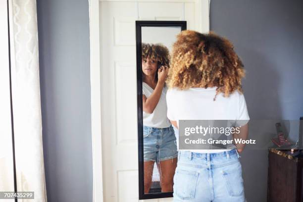 black woman examining hair in mirror - bedroom mirror stock-fotos und bilder