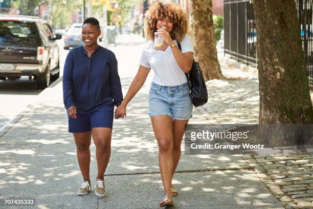 black women holding hands on city sidewalk - black shorts photos et images de collection