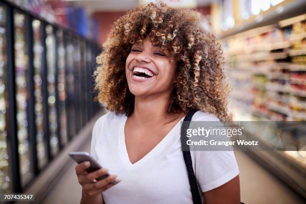 black woman holding cell phone laughing in grocery store - happy customer stock pictures, royalty-free photos & images