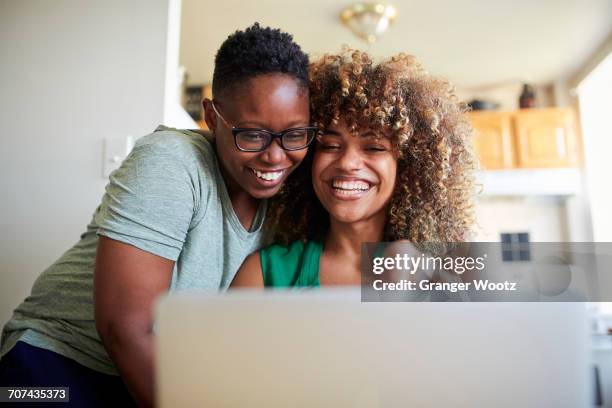 laughing black women hugging and using laptop - lesbian date stock-fotos und bilder