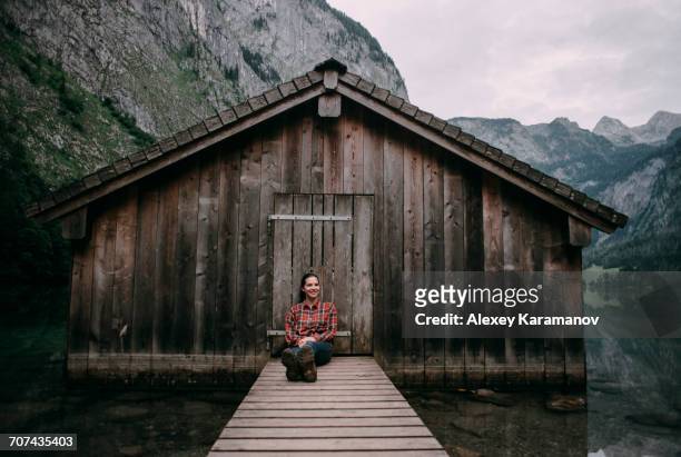 caucasian woman sitting on dock at remote cabin - cabin stock-fotos und bilder