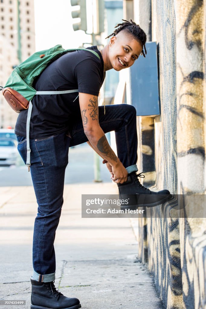 Androgynous Mixed Race woman carrying backpack adjusting boot