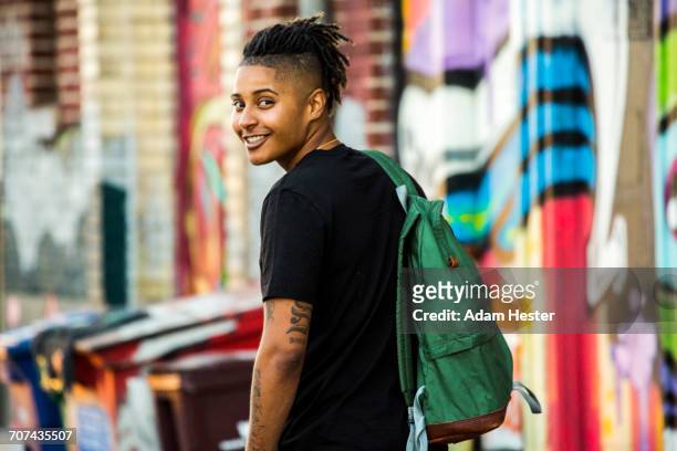 Portrait of smiling androgynous Mixed Race woman near on graffiti wall