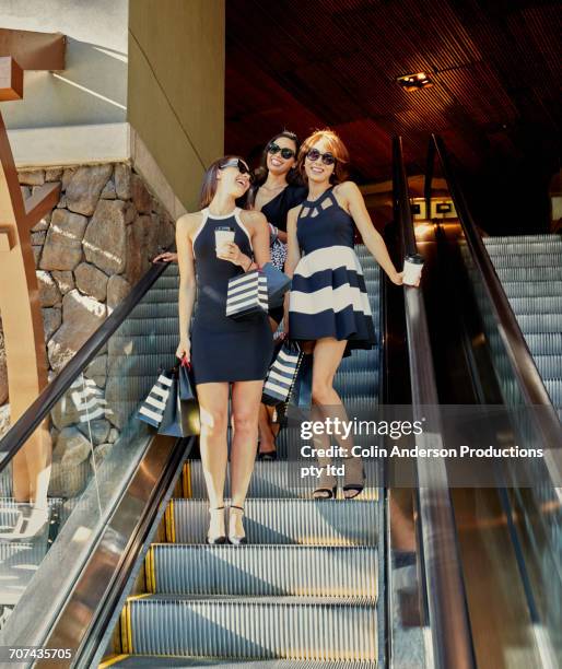 glamorous friends riding escalator in shopping mall - rico e anderson fotografías e imágenes de stock