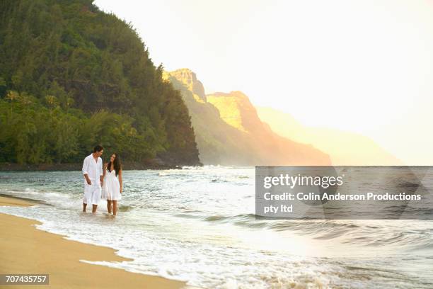 couple wading in ocean waves on sunny beach - hawaii scenics stock pictures, royalty-free photos & images
