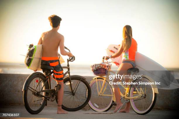 teenage boy and girl carrying surfboards on bicycles - teen boy barefoot stock pictures, royalty-free photos & images