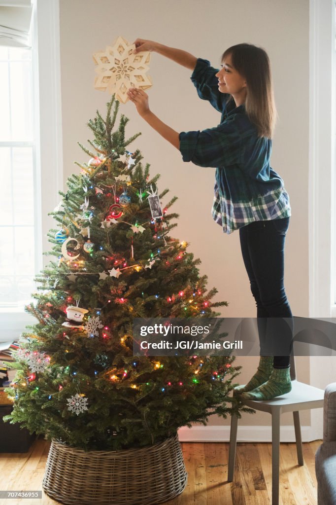 Mixed Race woman placing star ornament on top of Christmas tree