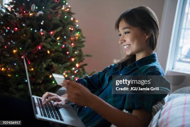 mixed race woman online shopping with laptop near christmas tree - weihnachten laptop stock-fotos und bilder