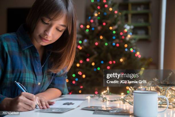 mixed race woman writing on card near christmas tree - correspondence stock pictures, royalty-free photos & images