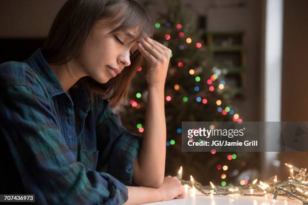 mixed race woman with headache near christmas tree - holiday sadness stock pictures, royalty-free photos & images