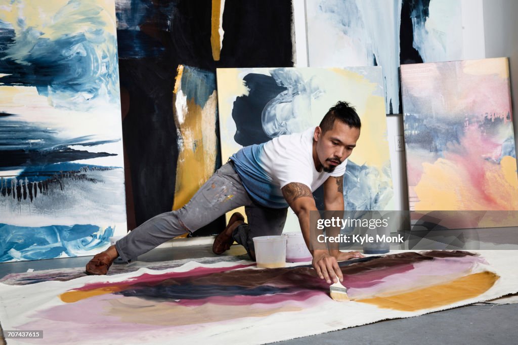 Pacific Islander artist kneeling on floor painting on canvas