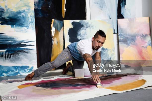 pacific islander artist kneeling on floor painting on canvas - artist imagens e fotografias de stock