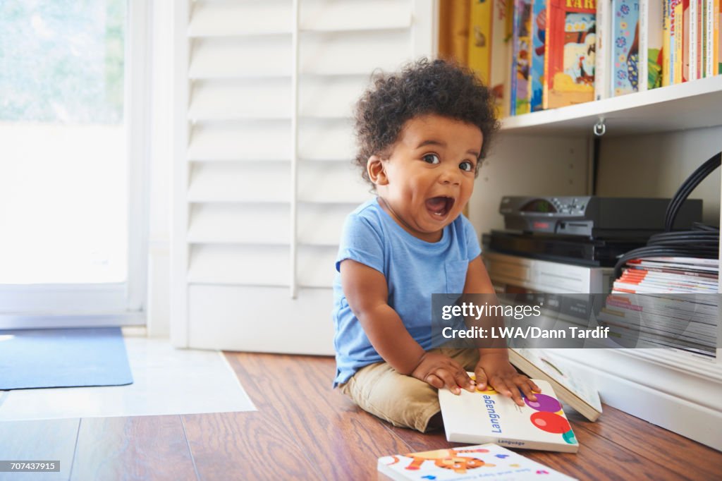 Surprised Black baby boy sitting on floor playing with books
