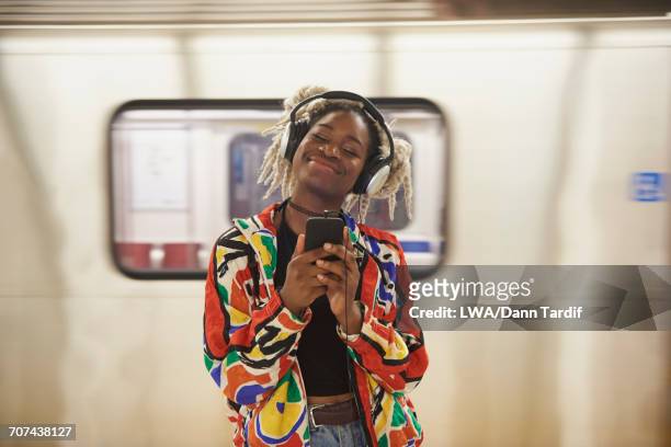 black woman listening to cell phone with headphones near subway - listening 個照片及圖片檔