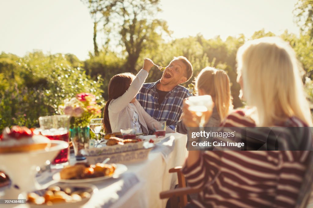 Playful daughter feeding father at sunny garden party patio table