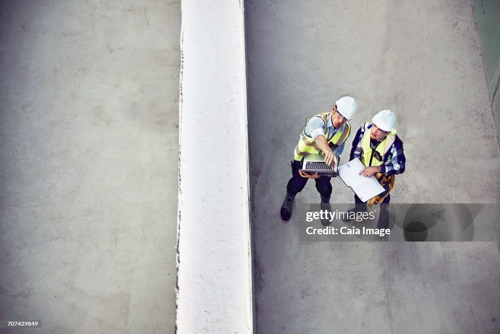 Construction worker and engineer with laptop talking at construction site