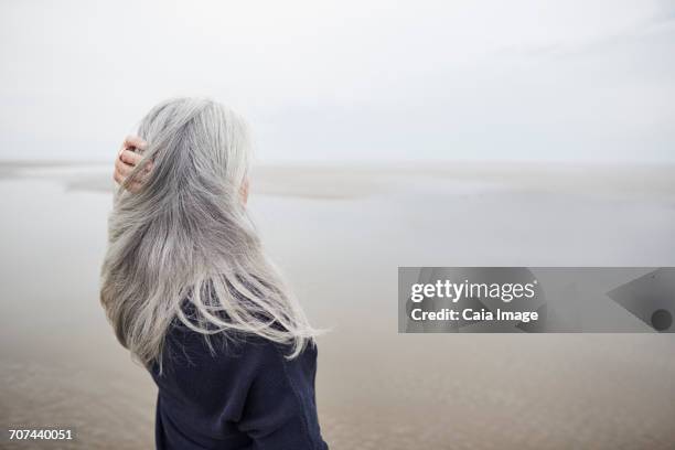 senior woman with hand in long gray hair on winter beach - une seule femme d'âge mûr photos et images de collection