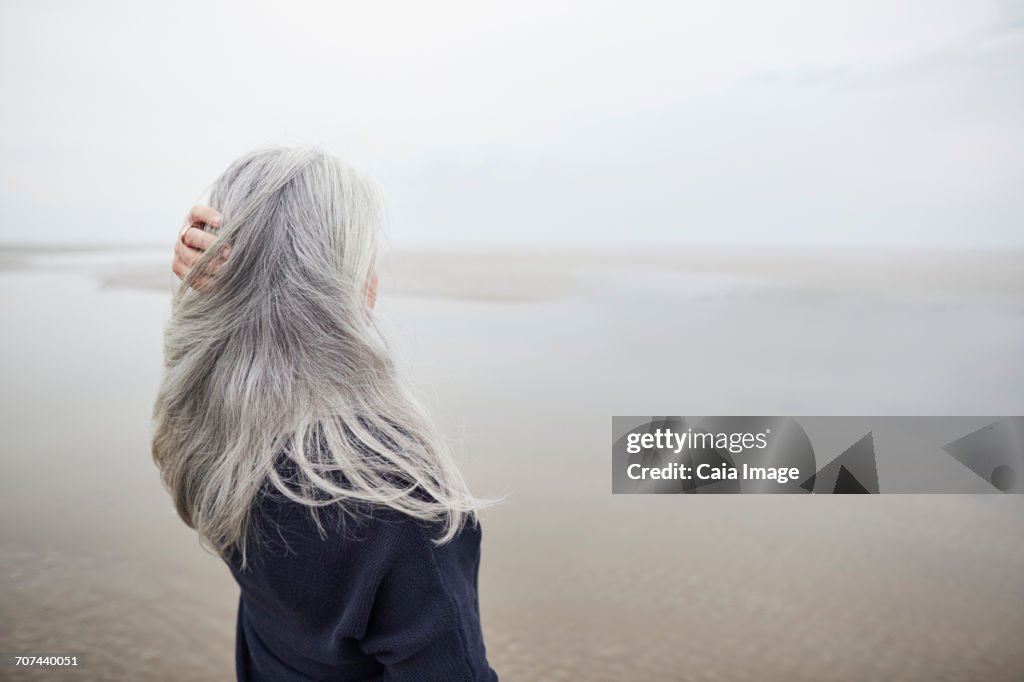 Senior woman with hand in long gray hair on winter beach