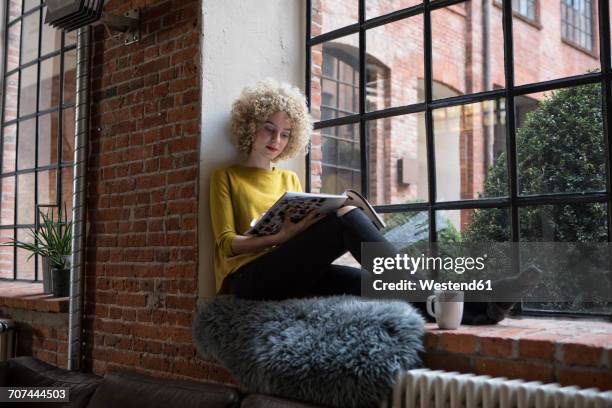young woman sitting on window sill - mujer revista fotografías e imágenes de stock