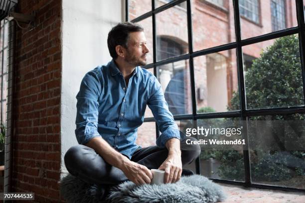 mature man sitting on window sill, relaxing with cup of coffee - ausblick stock-fotos und bilder
