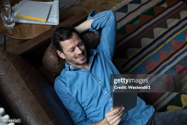 man lying on couch, using digital tablet - relaxing sofa stock-fotos und bilder