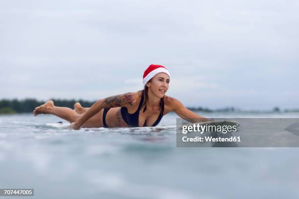 indonesia, bali, woman on surfboard wearing santa hat - surfing santa stock pictures, royalty-free photos & images