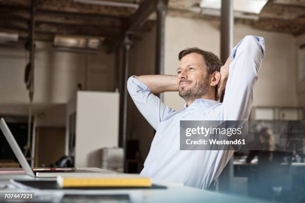 confident businessman at desk leaning back - homme content chez lui photos et images de collection