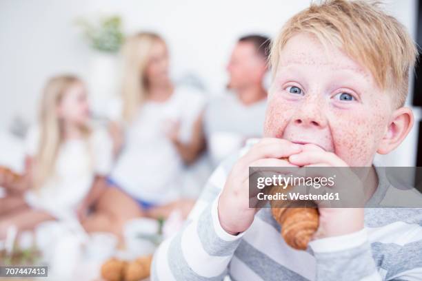 portrait of boy biting into croissant with family in background - young chubby girl photos et images de collection