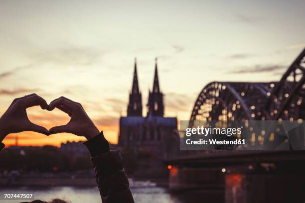 germany, cologne, woman shaping heart with her hands in front of cologne cathedral and hohenzollern bridge at dusk - köln - fotografias e filmes do acervo