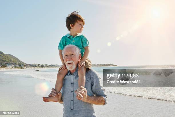 portrait of senior man with grandson on his shoulders on the beach - bära på axlarna bildbanksfoton och bilder