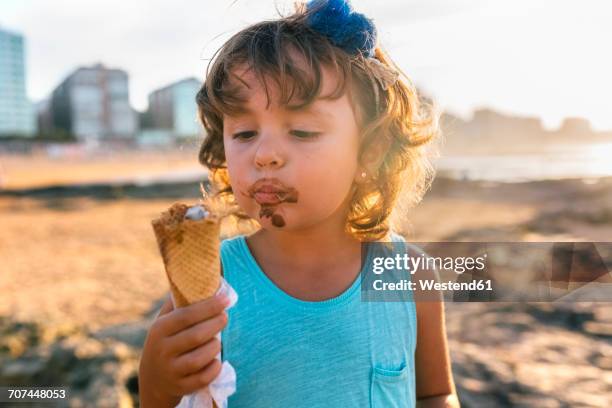 portrait of little girl eating chocolate icecream on the beach at sunset - girl eating messy ice cream cone stock pictures, royalty-free photos & images