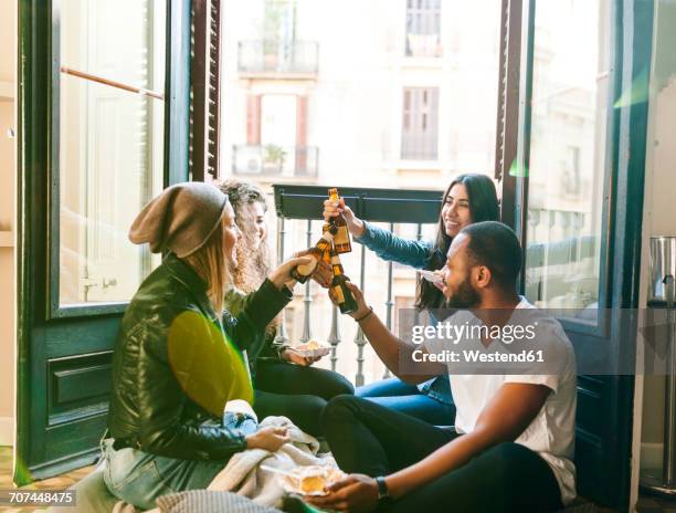 four friends clinking beer bottles - drinking alcohol at home stock pictures, royalty-free photos & images