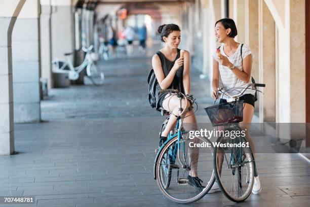 two young women with bicycles eating icecream - frau eistüte stock-fotos und bilder