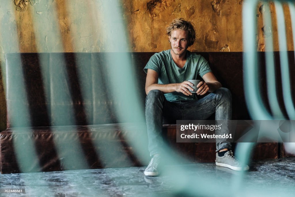 Man sitting on couch in unfinished room drinking cup of coffee