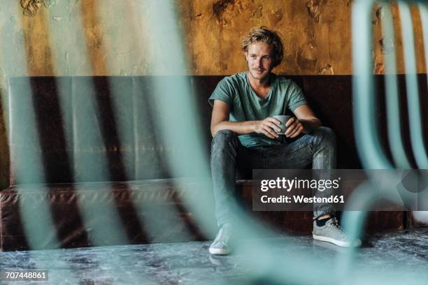 man sitting on couch in unfinished room drinking cup of coffee - founders cup portraits fotografías e imágenes de stock