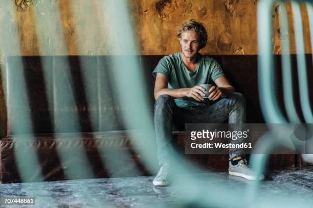 man sitting on couch in unfinished room drinking cup of coffee - focus on background stock pictures, royalty-free photos & images