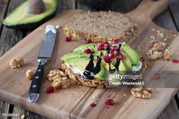 protein bread slice with cream cheese, sliced avocado, walnuts and pomegranate seed on wooden board - vollkornbrot stock-fotos und bilder