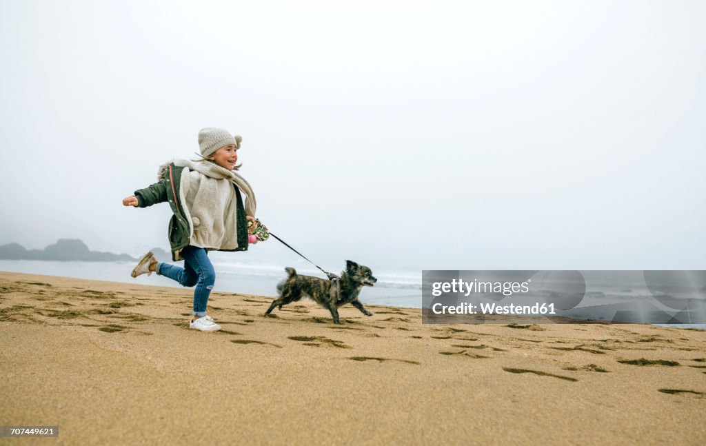 Happy girl running with dog on the beach on a foggy winter day