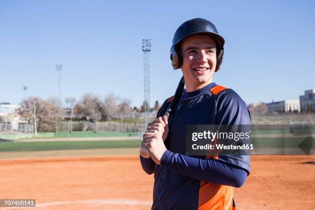 smiling baseball player holding a baseball bat - casque de baseball photos et images de collection