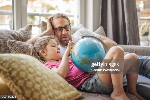 father and daughter lying with globe on sofa - genderblend stock pictures, royalty-free photos & images